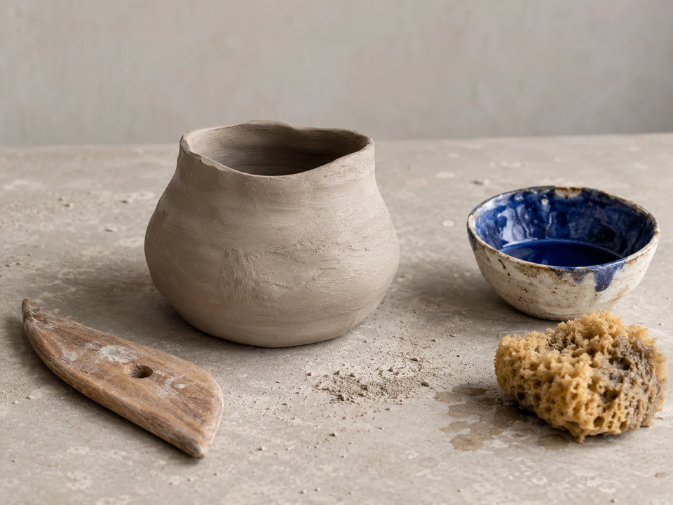 Clay vessels, a blue glazed bowl, and pottery tools on a studio workbench